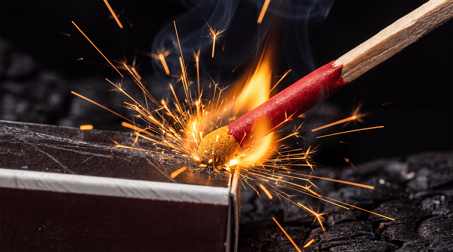 A stormproof match with a red stem and yellow head igniting against a striker in a shower of sparks